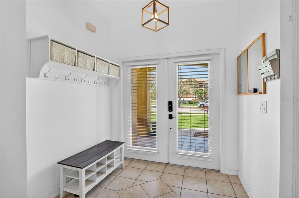 An entryway features a white storage bench, wall-mounted coat hooks with baskets, and double glass doors — 3809 AGUALINDA BOULEVARD, CAPE CORAL, FL