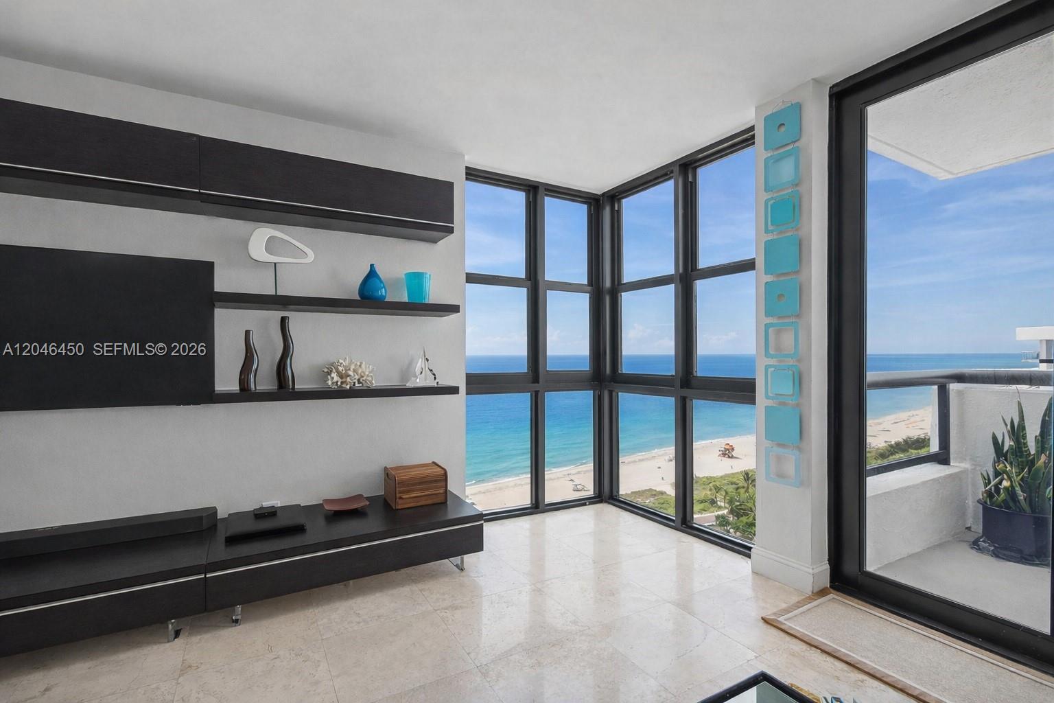 A living room features dark built-in shelving, a television, and floor-to-ceiling windows overlooking the ocean — 2555 Collins Ave # 1814, Miami Beach FL 33140, MIAMI BEACH, FL