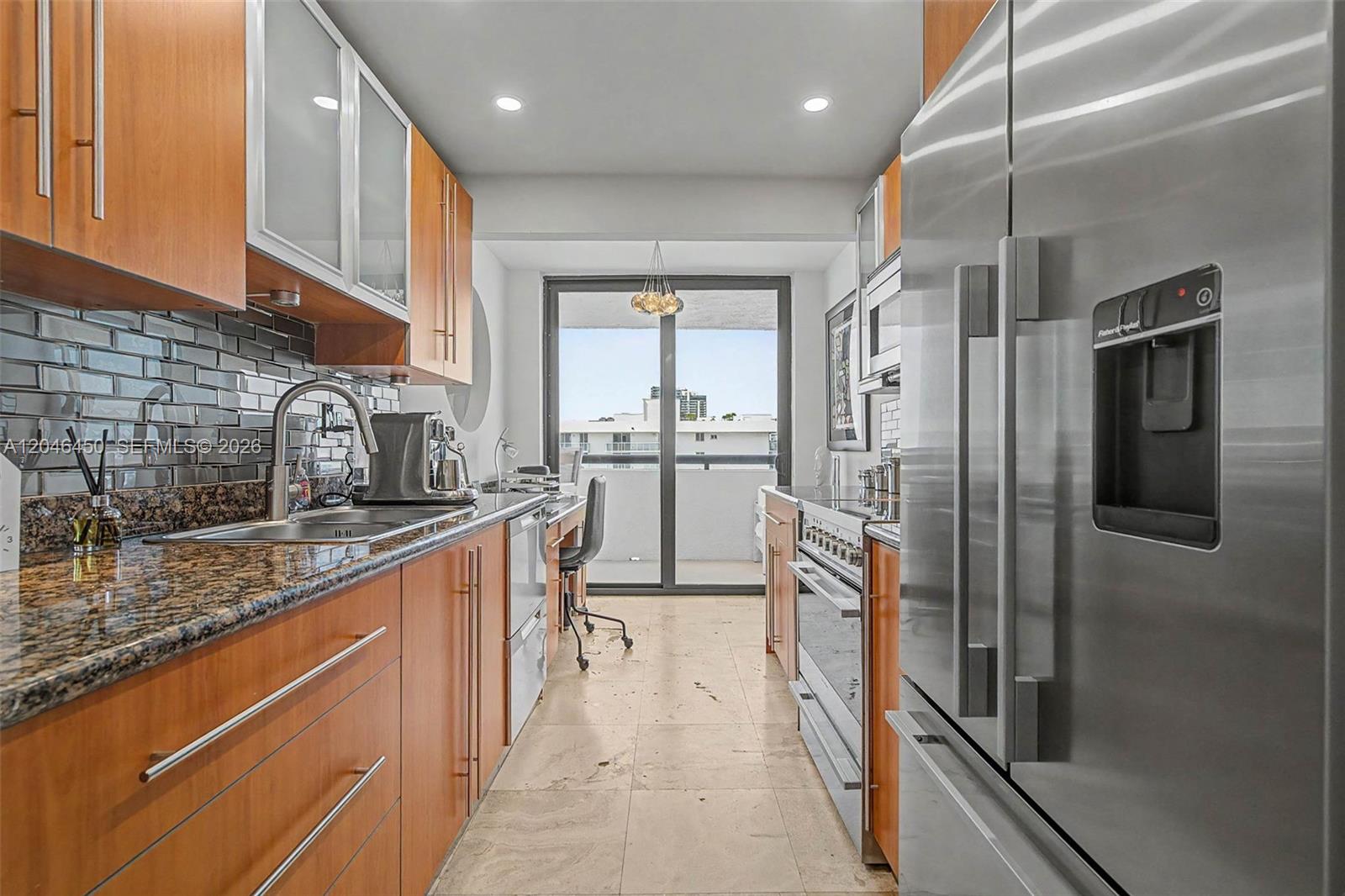 A galley kitchen features wood cabinets, granite countertops, stainless steel appliances, and a balcony view — 2555 Collins Ave # 1814, Miami Beach FL 33140, MIAMI BEACH, FL