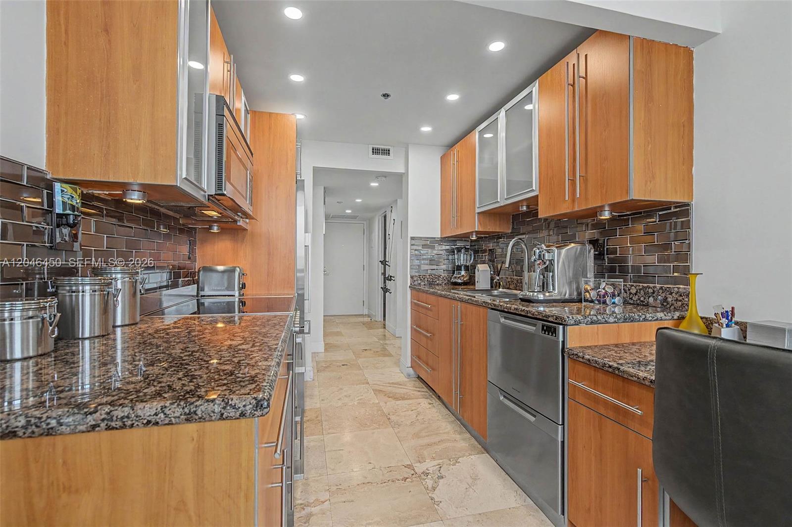 A galley kitchen features wood cabinets, granite countertops, stainless steel appliances, and tile flooring — 2555 Collins Ave # 1814, Miami Beach FL 33140, MIAMI BEACH, FL