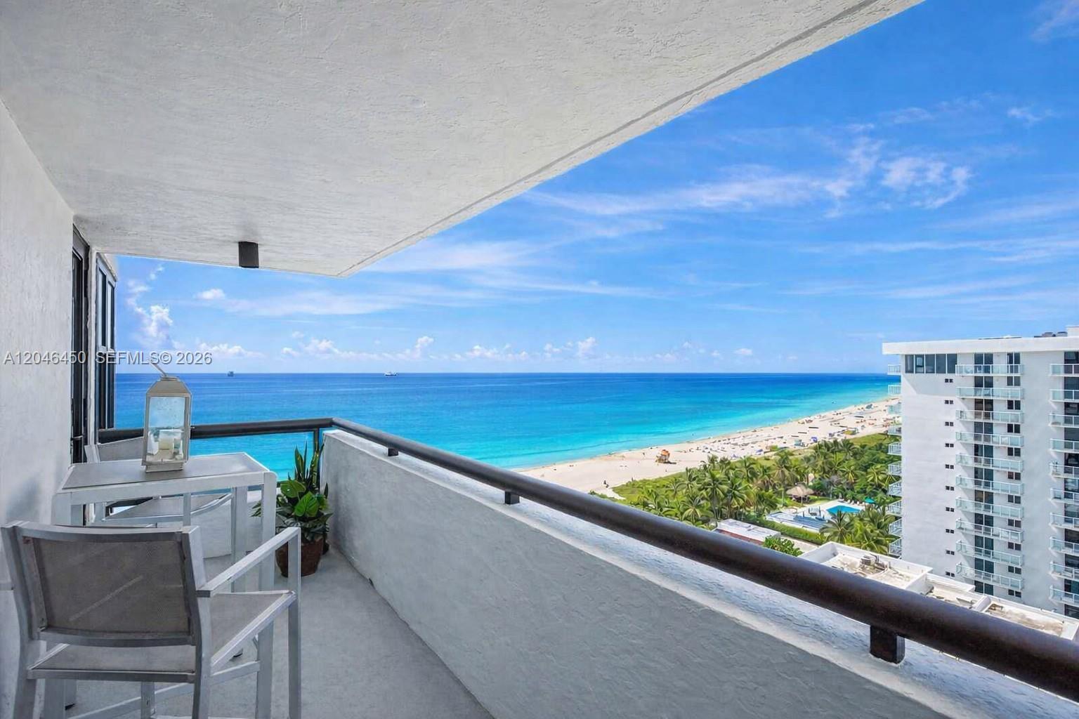 A balcony with a table and chairs overlooks the ocean and a sandy beach — 2555 Collins Ave # 1814, Miami Beach FL 33140, MIAMI BEACH, FL