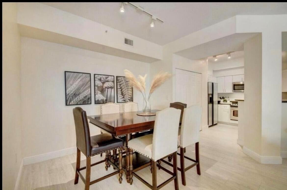 A dining area with a wooden table, upholstered chairs, and wall art leads to a kitchen — 802 W Windward Way # 216, Lantana FL 33462, LANTANA, FL