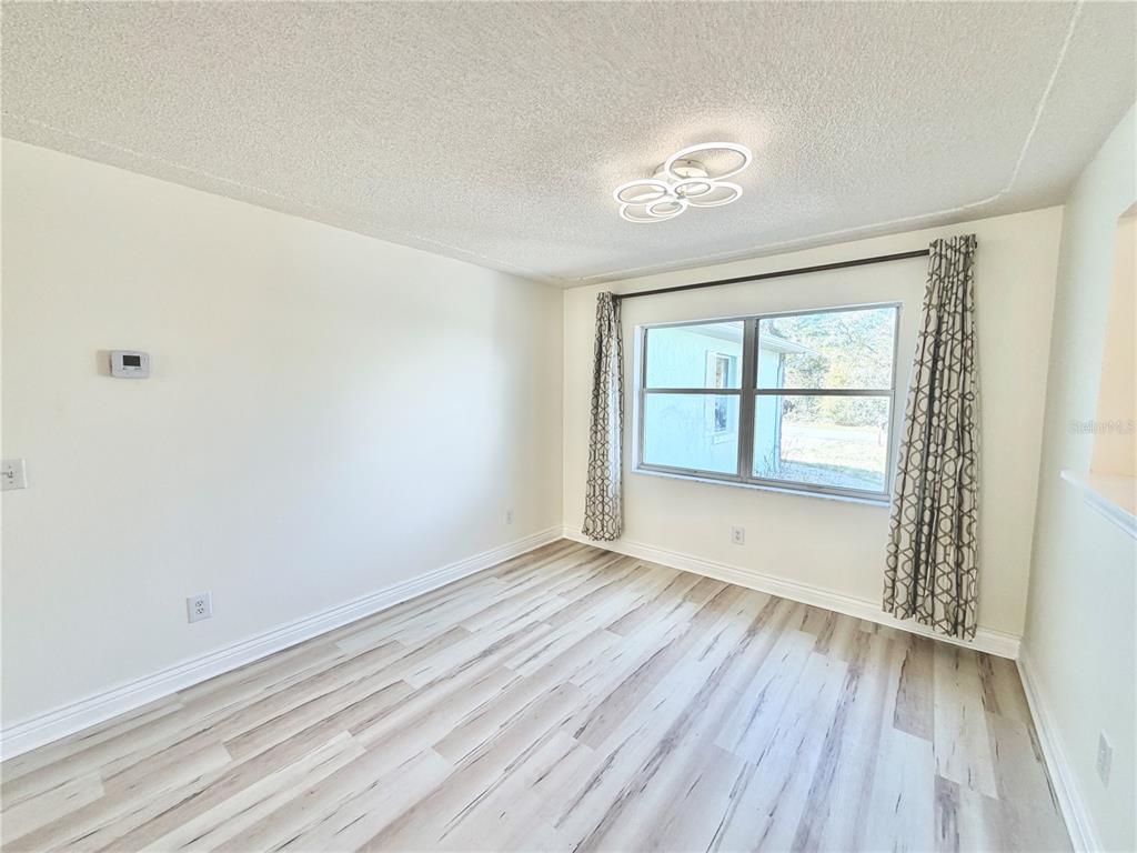 An empty room features light wood-look flooring, white walls, a window with curtains, and lighting — 17469 SW 35TH AVENUE ROAD, OCALA, FL