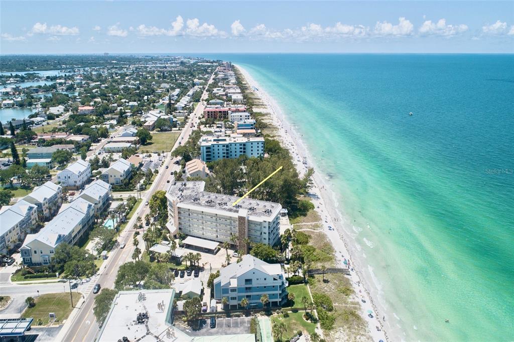 An aerial view shows a multi-story beachfront condominium building along a coastline with turquoise water — 2504 GULF BOULEVARD UNIT 304, INDIAN ROCKS BEACH, FL