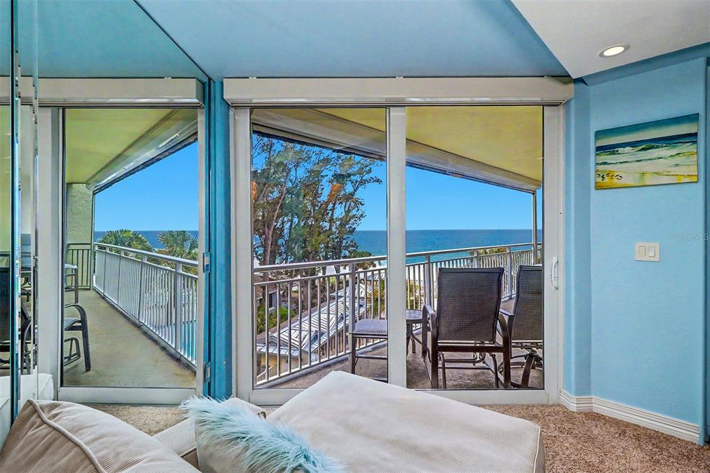 A bedroom with blue walls, carpet, and sliding glass doors opening to an oceanfront balcony — 2504 GULF BOULEVARD UNIT 304, INDIAN ROCKS BEACH, FL