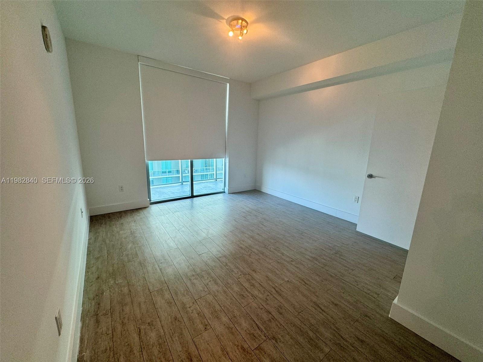 An empty room features light wood-look flooring, white walls, a ceiling light, and a balcony door — 79 SW 12th St, Miami FL 33130, MIAMI, FL