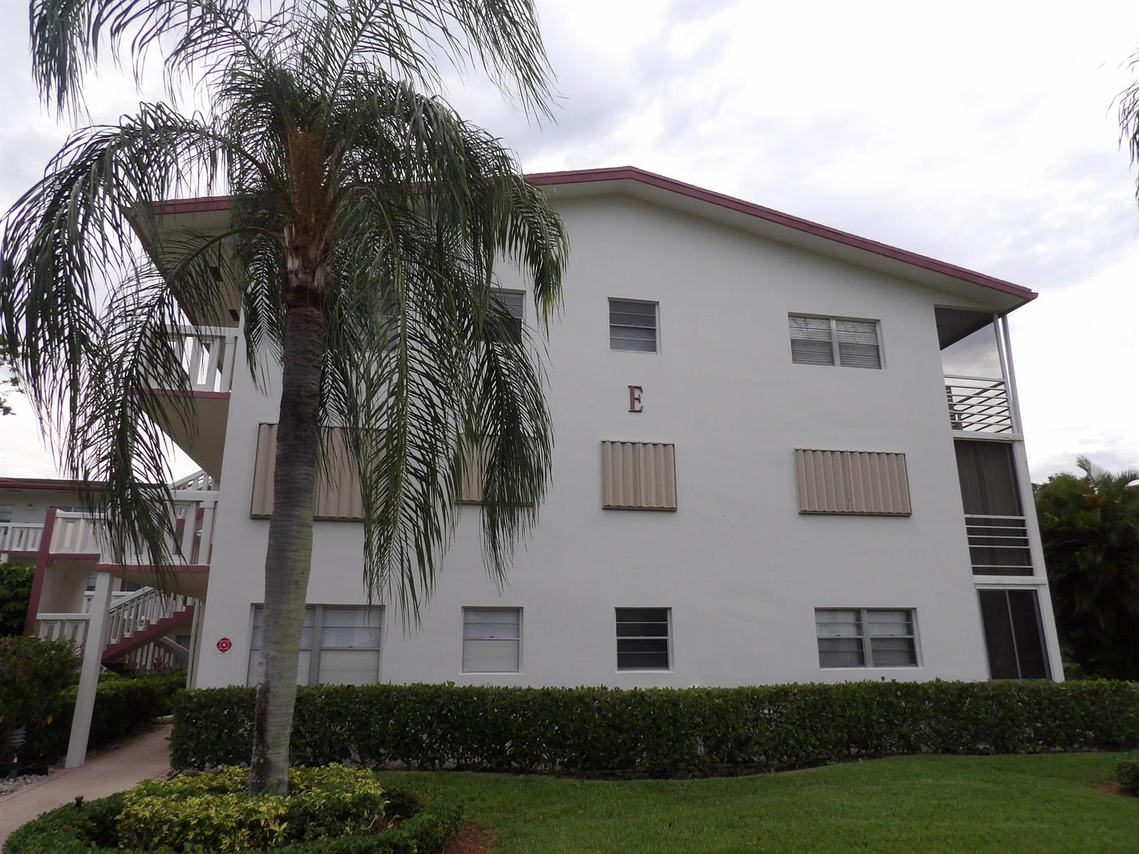 A three-story apartment building exterior features a palm tree, a letter E, and metal shutters — 195 Fanshaw Way E, Boca Raton FL 33434, BOCA RATON, FL