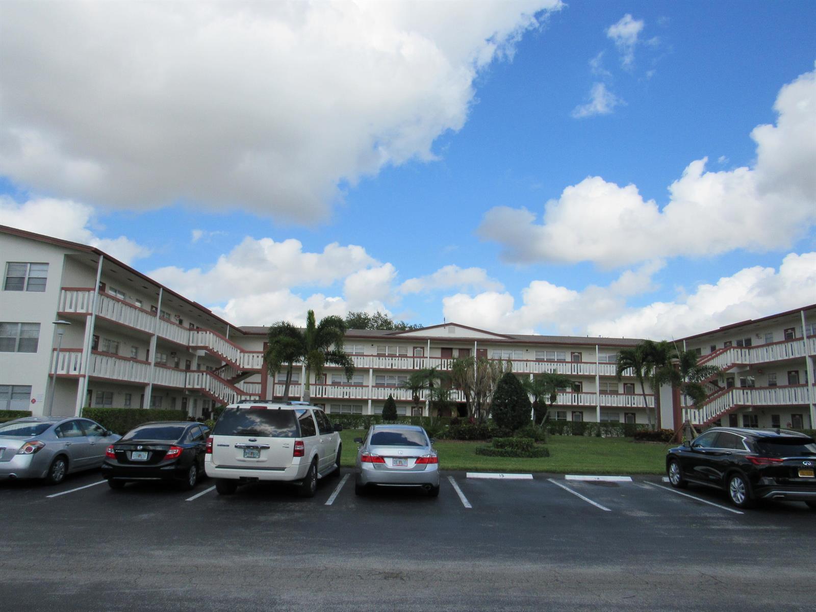 A multi-story apartment complex with exterior walkways and a parking lot in the foreground — 195 Fanshaw Way E, Boca Raton FL 33434, BOCA RATON, FL