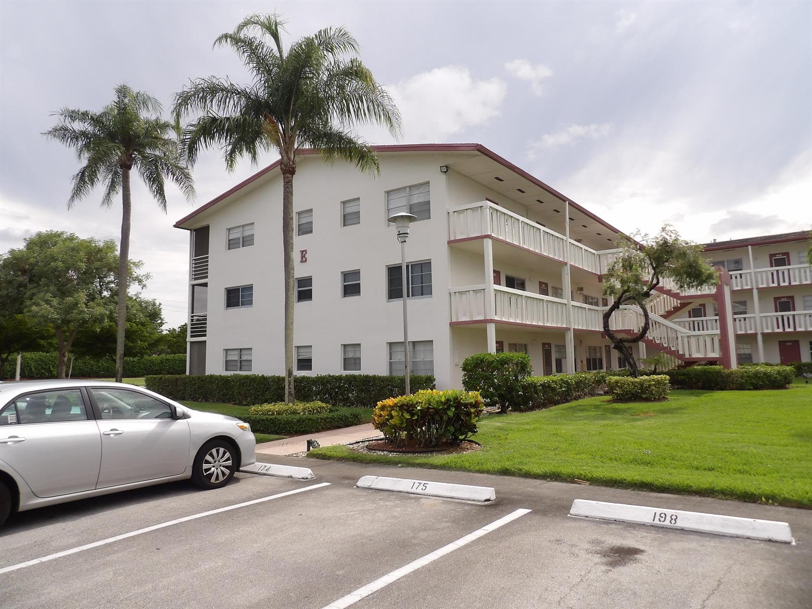 A three-story apartment building with white exterior walls and balconies sits behind a parking lot — 195 Fanshaw Way E, Boca Raton FL 33434, BOCA RATON, FL