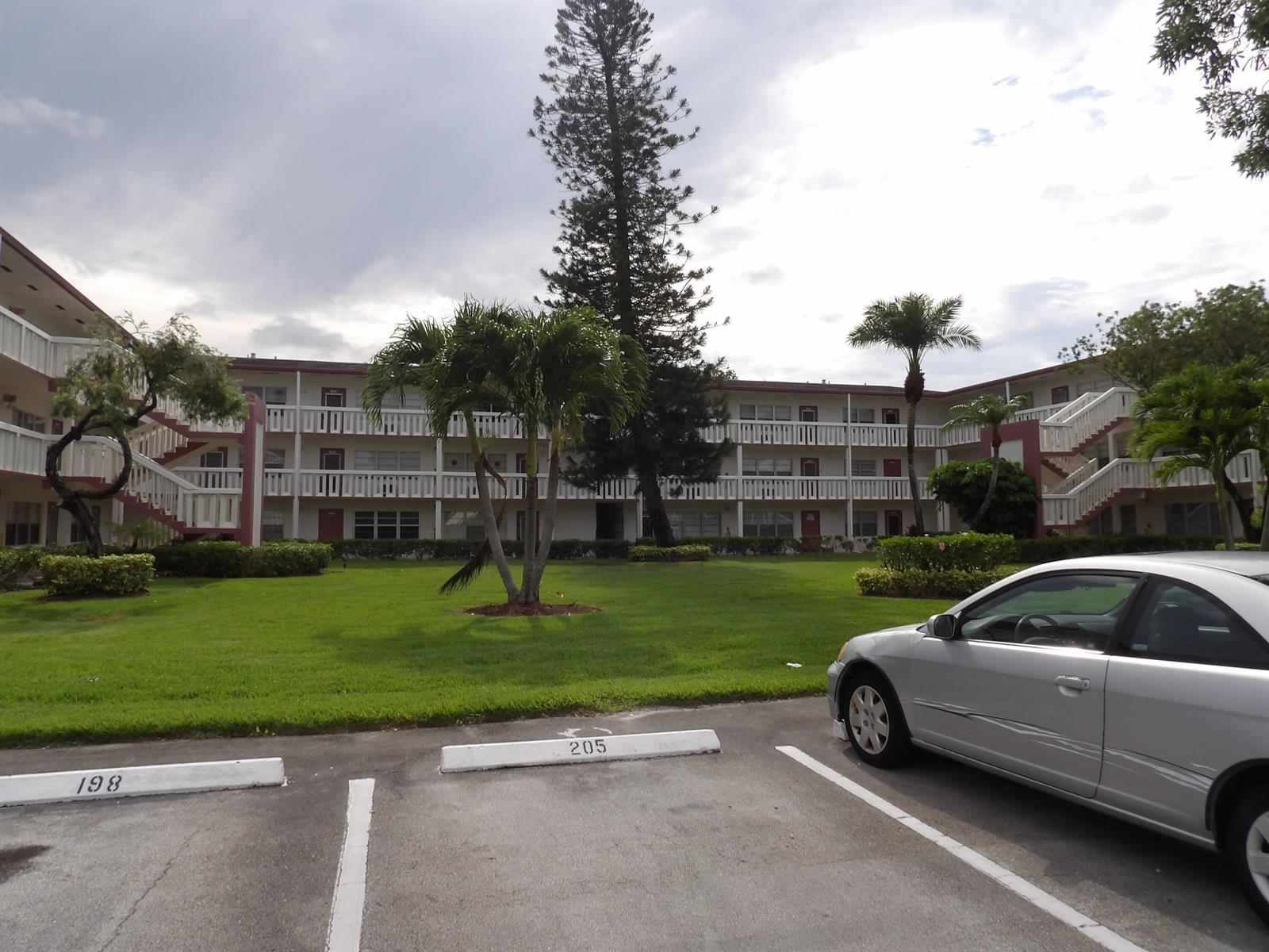 A multi-story apartment building with exterior walkways, palm trees, and a parking lot in front — 195 Fanshaw Way E, Boca Raton FL 33434, BOCA RATON, FL