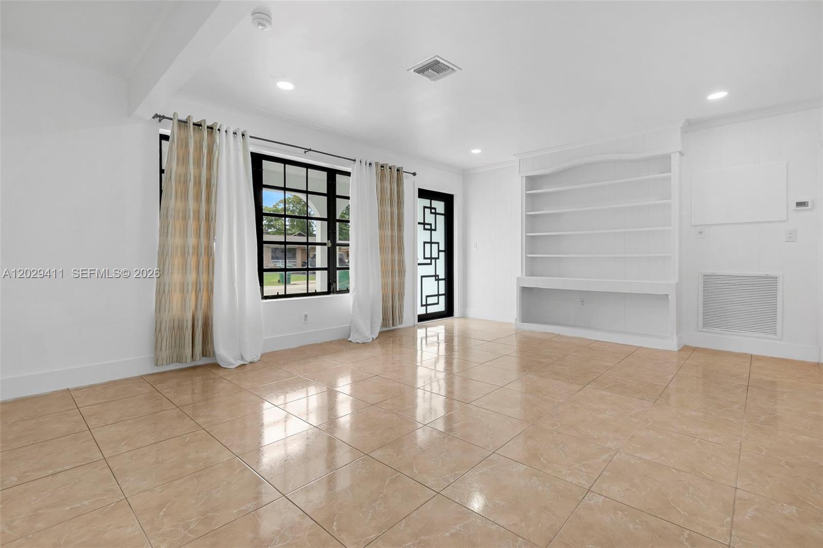 A bright living room features light tile flooring, white walls, built-in shelving, and large windows — 6101 SW 24th St # 1, Miramar FL 33023, MIRAMAR, FL