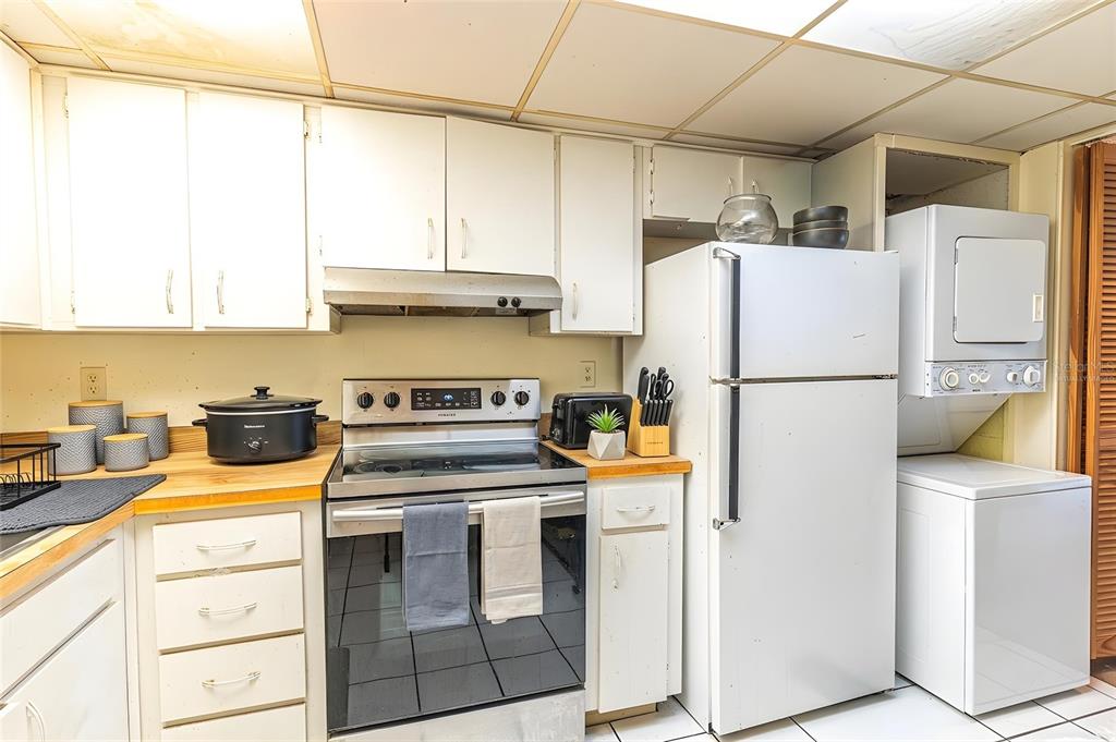 A kitchen features white cabinets, a stainless steel stove, a refrigerator, and a stacked washer-dryer — 709 RUSSELL LANE UNIT 222, BRANDON, FL