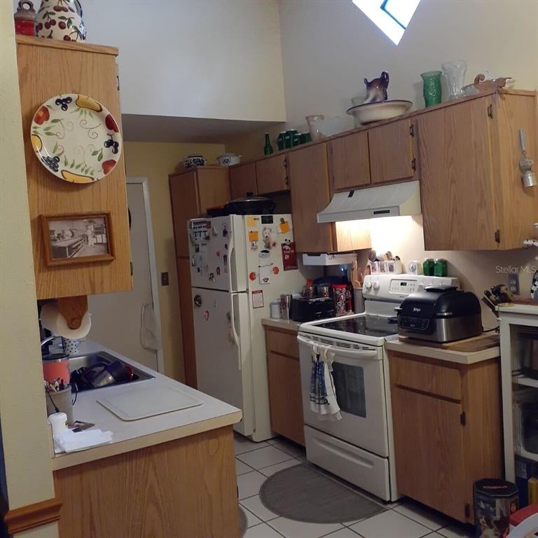 A kitchen features oak cabinets, white appliances, tiled floors, and a vaulted ceiling — 13427 LARAWAY DRIVE, RIVERVIEW, FL