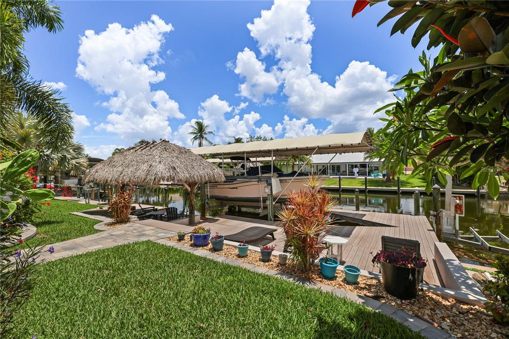 A backyard features a boat lift, a thatched-roof tiki hut, and a wooden deck — 5215 PELICAN BOULEVARD, CAPE CORAL, FL