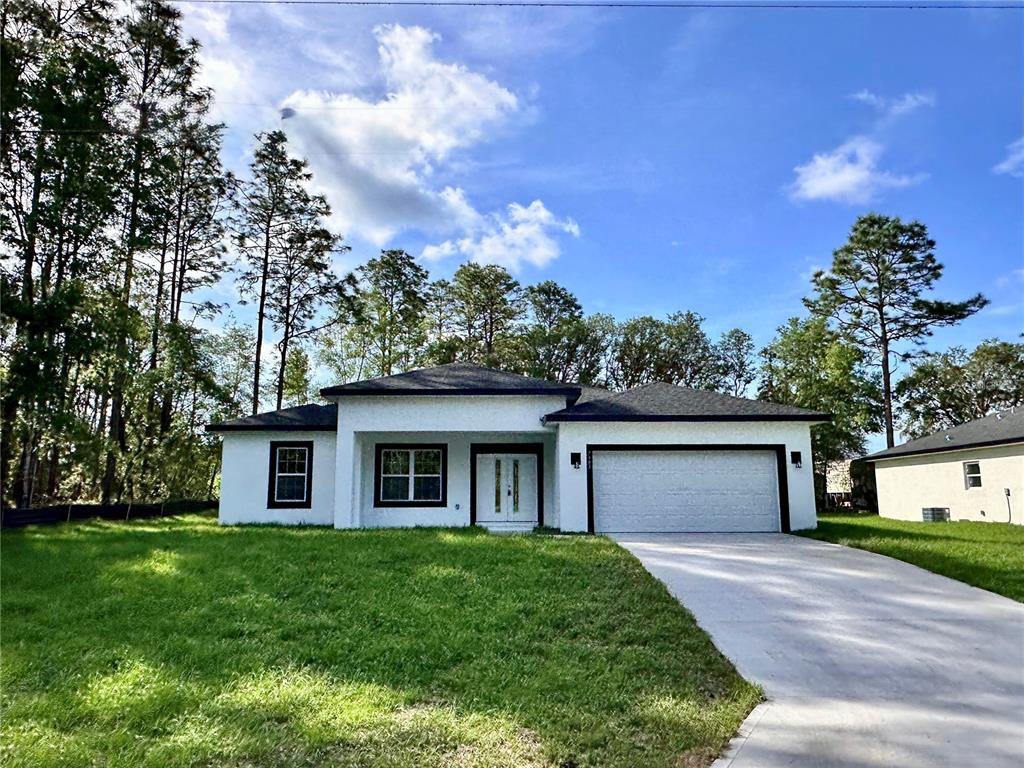 A single-story white house with a two-car garage sits on a grassy lot with trees — 7983 N POCONO DRIVE, CITRUS SPRINGS, FL