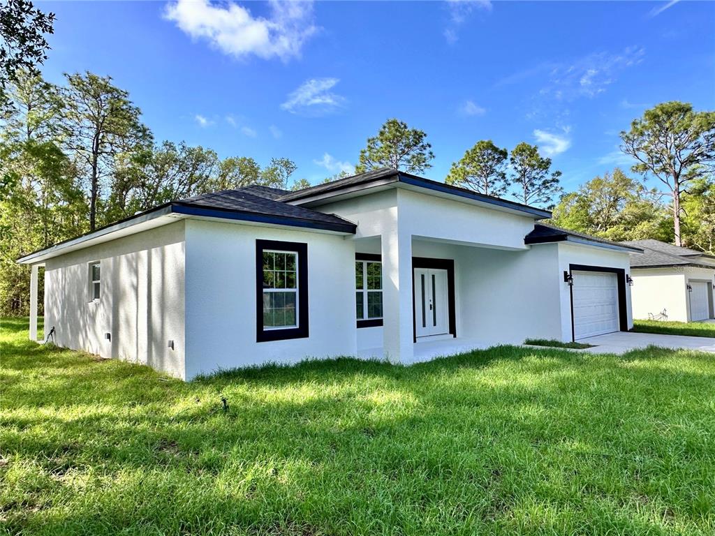 A white single-story house with a black-trimmed front door and windows sits on a grassy lot — 7983 N POCONO DRIVE, CITRUS SPRINGS, FL