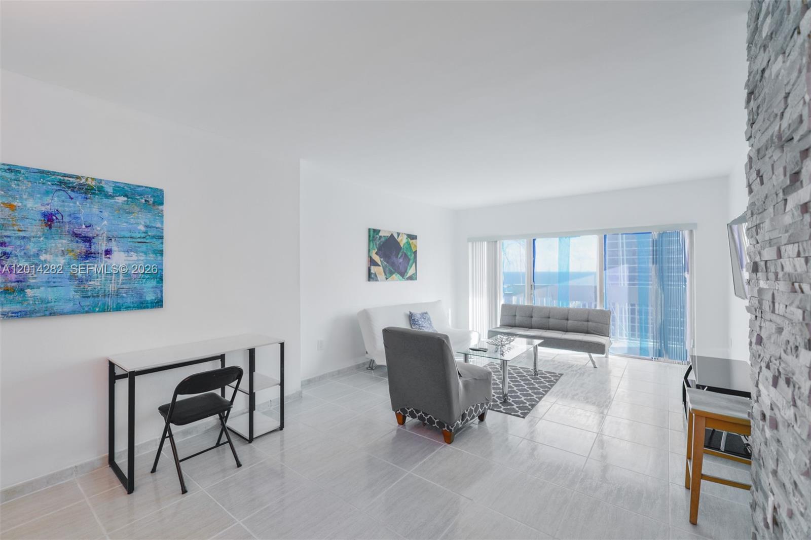 A living room features white walls, tile flooring, a stone accent wall, and balcony access — 1950 S Ocean Dr # 17N, Hallandale Beach FL 33009, HALLANDALE BEACH, FL