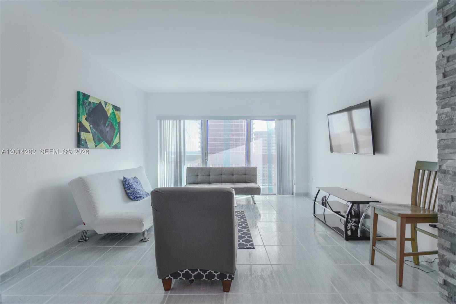 A living room features white walls, tile flooring, a mounted television, and modern furniture — 1950 S Ocean Dr # 17N, Hallandale Beach FL 33009, HALLANDALE BEACH, FL