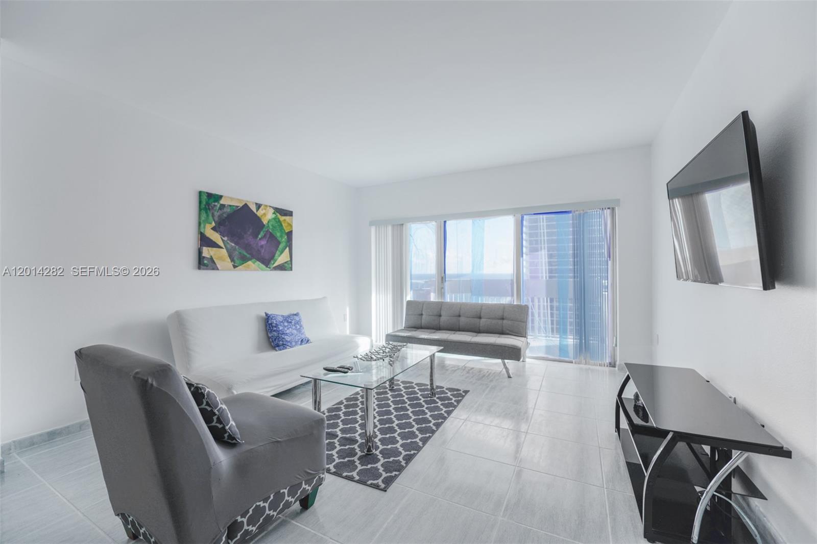 A living room features white walls, tile flooring, two sofas, an armchair, and a television — 1950 S Ocean Dr # 17N, Hallandale Beach FL 33009, HALLANDALE BEACH, FL