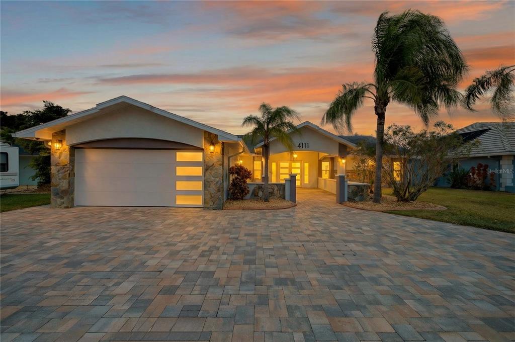 A single-story house with a paved driveway, stone accents, and a two-car garage at sunset — 4111 MARINE PARKWAY, NEW PORT RICHEY, FL