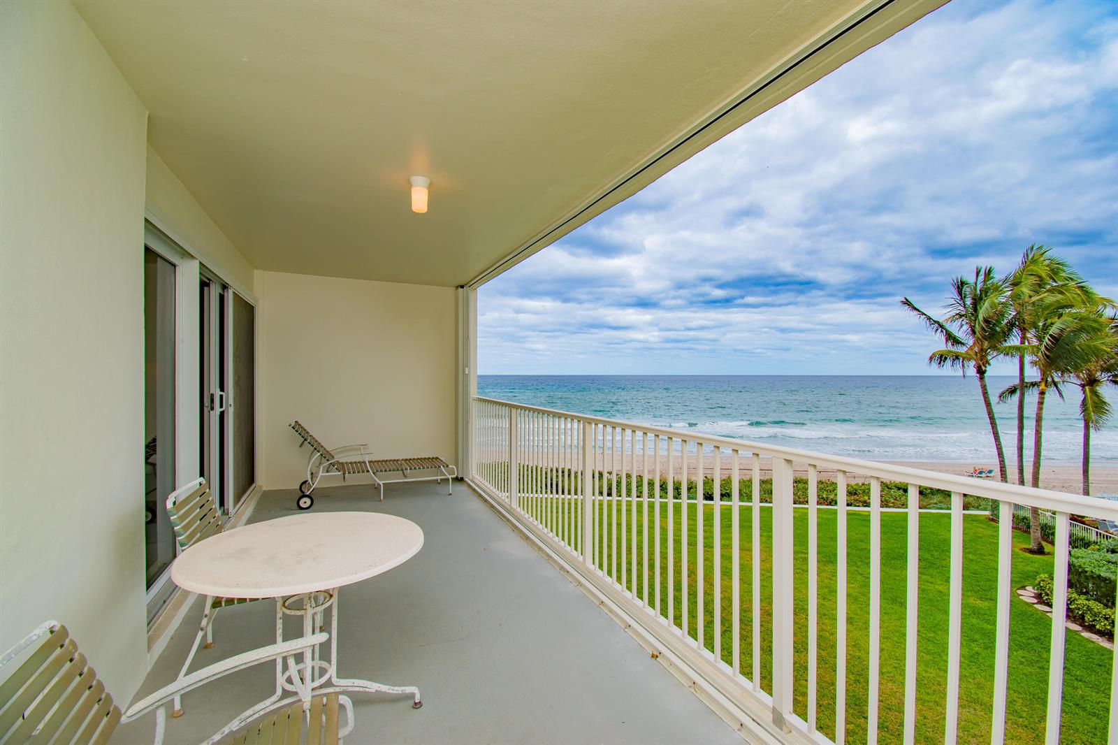 A balcony with a table and chairs overlooks a grassy lawn, beach, and the ocean — 3101 S Ocean Boulevard # 322, Highland Beach FL 33487, HIGHLAND BEACH, FL