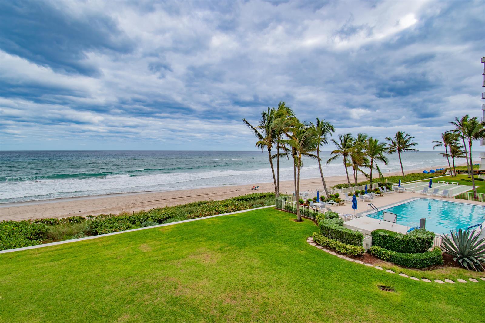 An elevated view of a swimming pool, palm trees, and a sandy beach by the ocean — 3101 S Ocean Boulevard # 322, Highland Beach FL 33487, HIGHLAND BEACH, FL