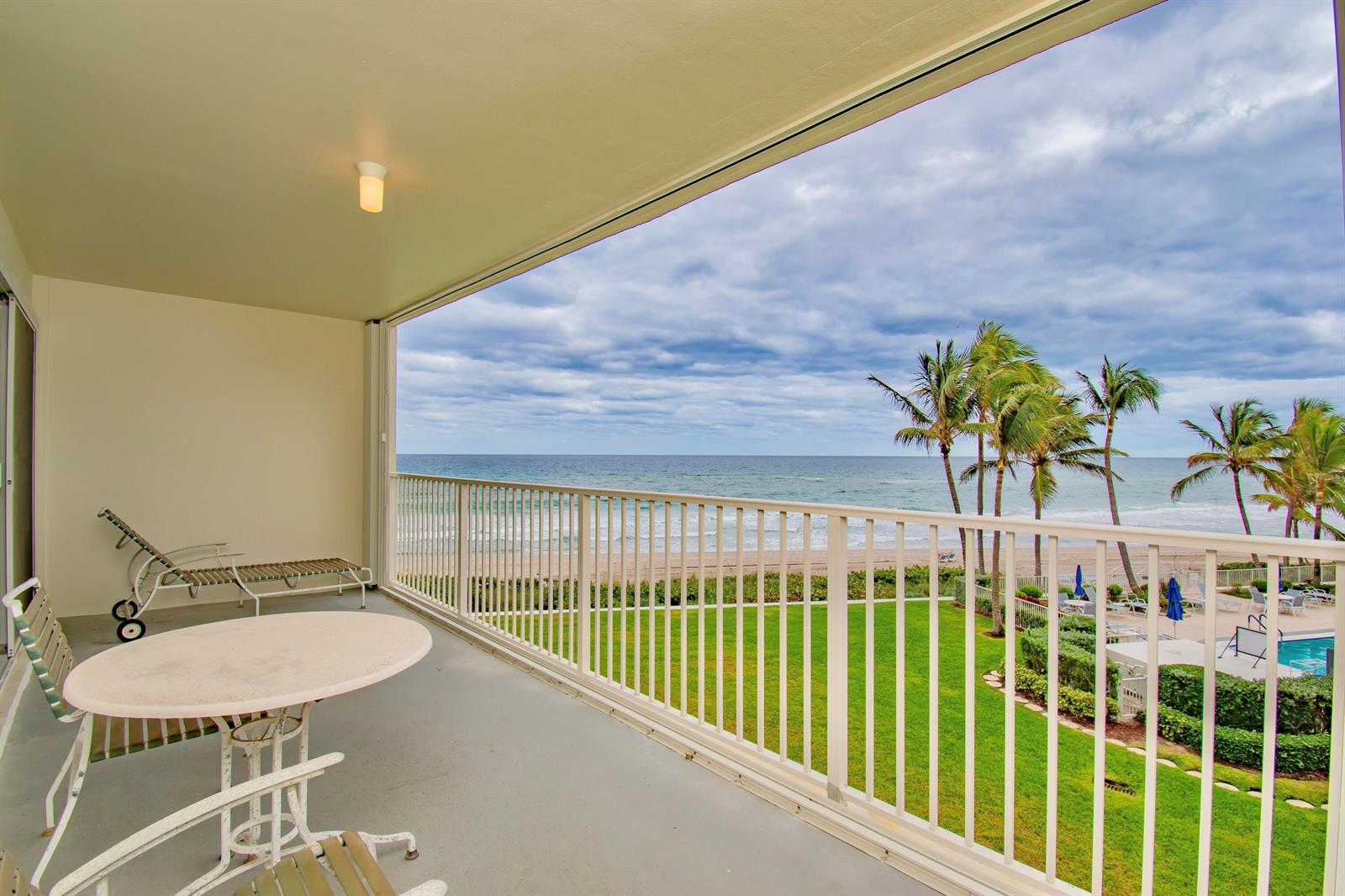 A balcony with a table and lounge chair overlooks a grassy lawn, beach, and ocean — 3101 S Ocean Boulevard # 322, Highland Beach FL 33487, HIGHLAND BEACH, FL