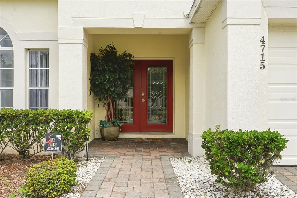 A paved walkway leads to a red double front door under a covered entryway — 4715 CUMBRIAN LAKES DRIVE, KISSIMMEE, FL