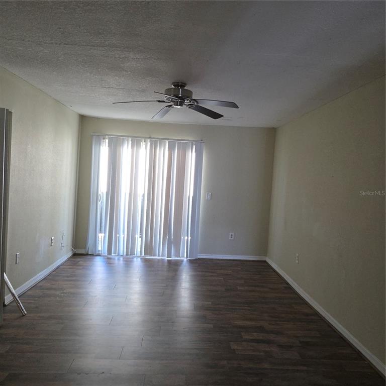 An empty room features wood-look flooring, beige walls, a ceiling fan, and vertical window blinds — 922 LAKE DESTINY ROAD UNIT F, ALTAMONTE SPRINGS, FL