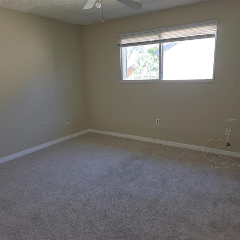 An empty bedroom features beige walls, light-colored carpeting, a ceiling fan, and a window — 922 LAKE DESTINY ROAD UNIT F, ALTAMONTE SPRINGS, FL