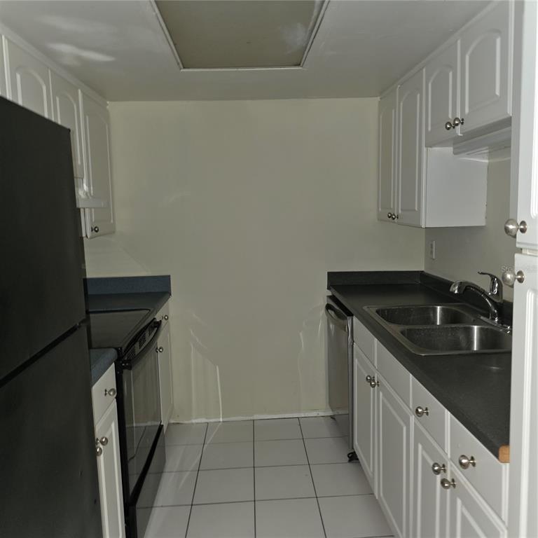 A galley kitchen features white cabinets, black appliances, dark countertops, and white tile flooring — 922 LAKE DESTINY ROAD UNIT F, ALTAMONTE SPRINGS, FL