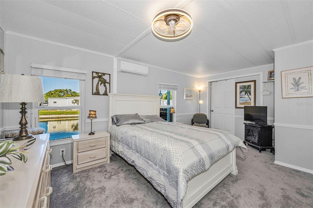 A bedroom features a white bed, gray carpet, a ceiling fan, and a waterfront view — 4454 TUCKER SQUARE, NEW PORT RICHEY, FL