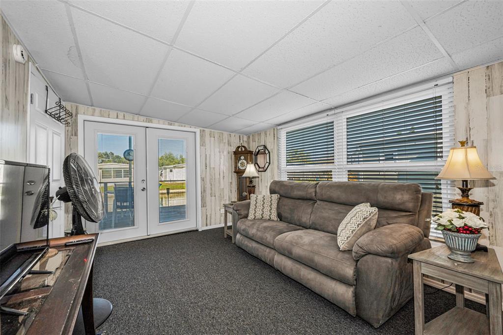 A living room features gray carpet, wood-paneled walls, a brown sofa, and glass patio doors — 4454 TUCKER SQUARE, NEW PORT RICHEY, FL