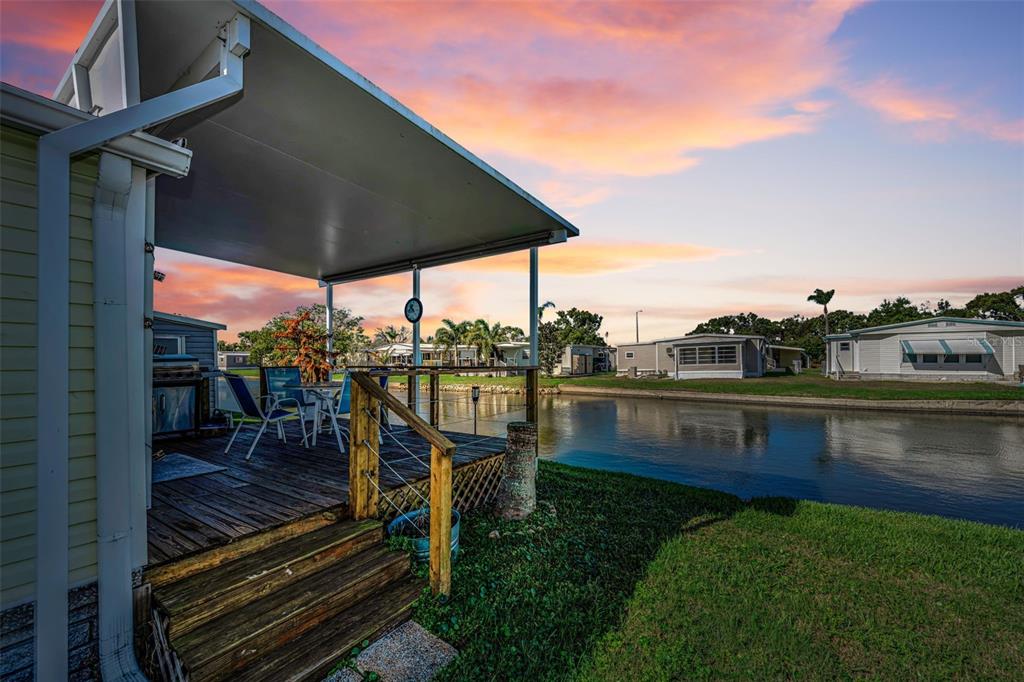 A wooden deck with patio furniture overlooks a canal at sunset next to a house — 4454 TUCKER SQUARE, NEW PORT RICHEY, FL
