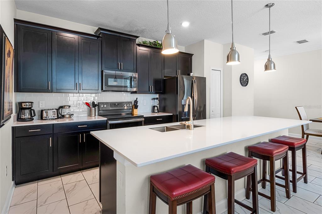 A kitchen features dark cabinetry, white countertops, a large island with bar stools, and appliances — 1224 CHALLENGE DRIVE, DAVENPORT, FL