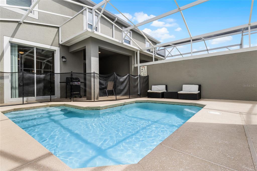A swimming pool with a safety fence sits on a patio enclosed by a screen — 1224 CHALLENGE DRIVE, DAVENPORT, FL