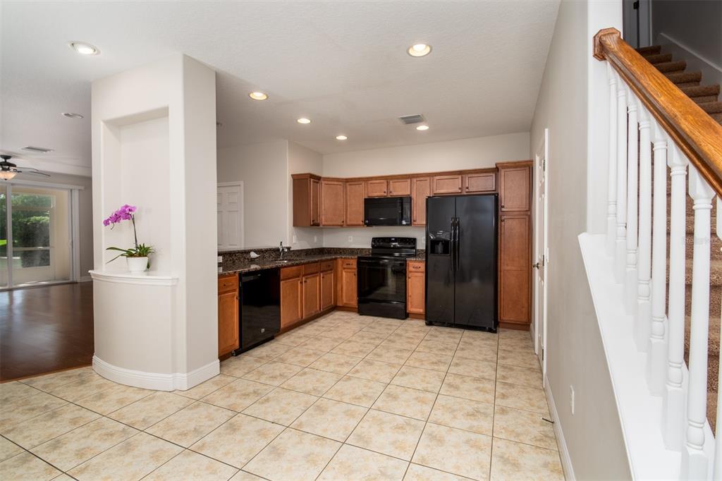 A kitchen with wood cabinets, black appliances, granite countertops, and tile flooring near a staircase — 403 HARBOR RIDGE DRIVE, PALM HARBOR, FL