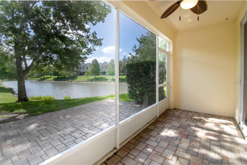 A screened-in patio with paver flooring overlooks a lake and green space — 403 HARBOR RIDGE DRIVE, PALM HARBOR, FL