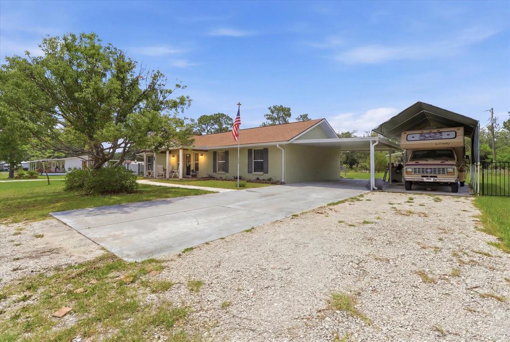 A single-story house with a gravel driveway, attached carport, and a parked recreational vehicle — 6928 W HAMILL COURT, HOMOSASSA, FL
