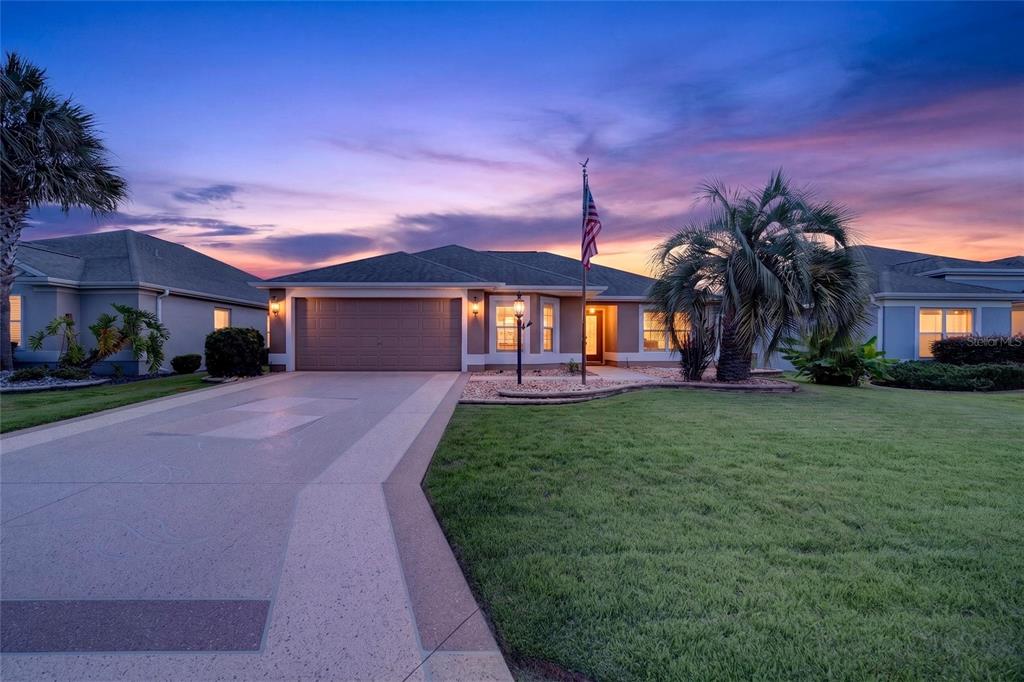 A single-story house with a two-car garage, a flag pole, and palm trees at dusk — 726 BRADFORD LOOP, THE VILLAGES, FL