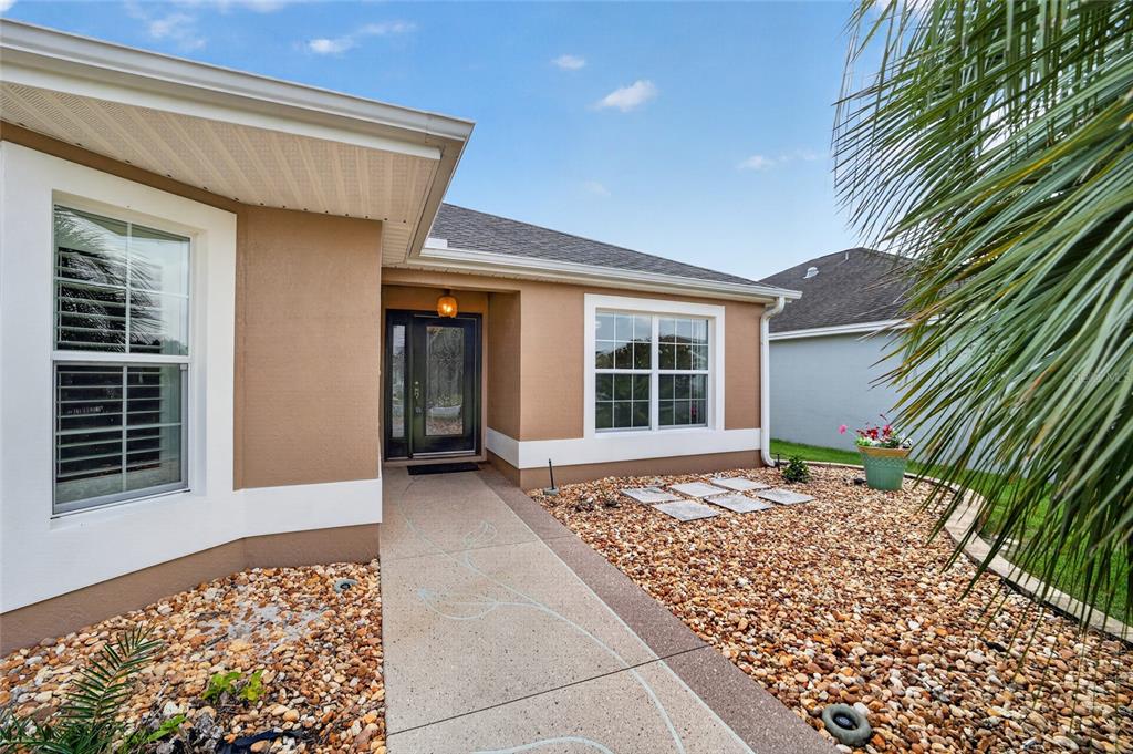 The exterior of a tan house features a concrete walkway leading to a dark front door — 726 BRADFORD LOOP, THE VILLAGES, FL