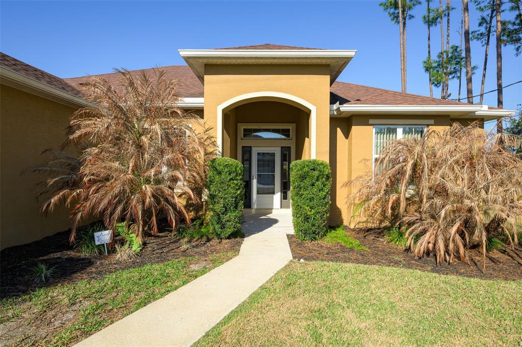 The front exterior of a tan house features a covered entryway with two large palm trees — 3 LAKE CHARLES PLACE, PALM COAST, FL