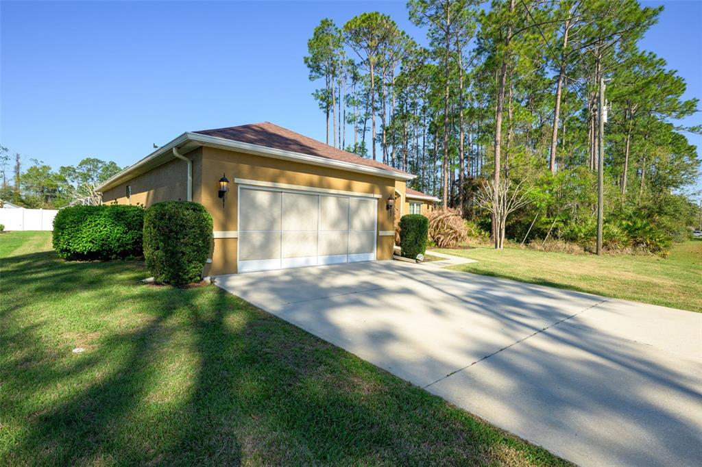 A tan house with a three-car garage and a concrete driveway sits on a grassy lot — 3 LAKE CHARLES PLACE, PALM COAST, FL