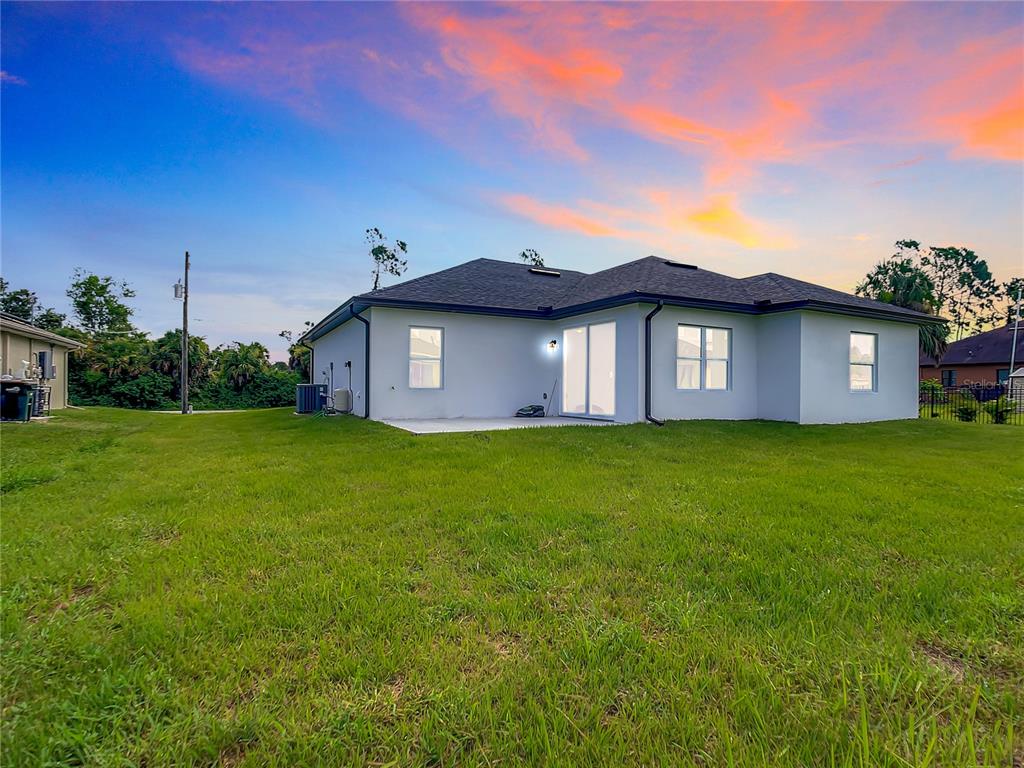 The rear exterior of a single-story house features a concrete patio and a grassy yard — 2109 NORDENDALE BOULEVARD, NORTH PORT, FL