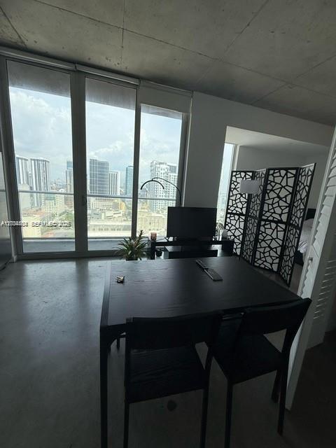 A dining area with a dark table and chairs sits before floor-to-ceiling windows overlooking city buildings — 151 SE 1st St # 2906, Miami FL 33131, MIAMI, FL