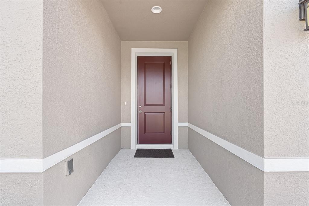 A covered entryway features a red front door, light-colored stucco walls, and a concrete floor — 2964 SLOUGH CREEK DRIVE, KISSIMMEE, FL