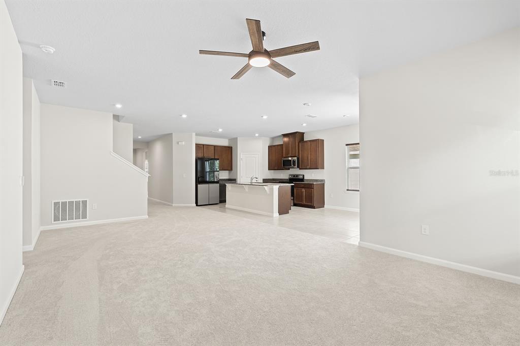 An open-concept living area features beige carpeting, a ceiling fan, and a kitchen with dark cabinetry — 2964 SLOUGH CREEK DRIVE, KISSIMMEE, FL
