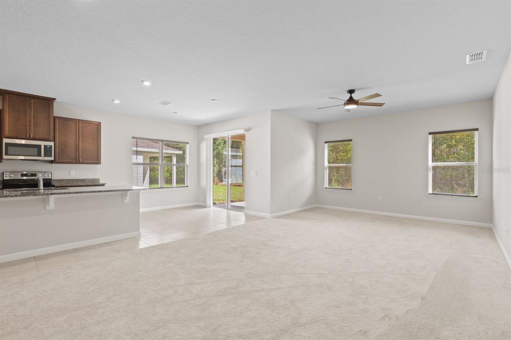 A spacious living room with beige carpet, a ceiling fan, and an adjacent kitchen area — 2964 SLOUGH CREEK DRIVE, KISSIMMEE, FL