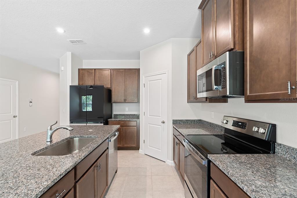 A kitchen features granite countertops, dark wood cabinets, stainless steel appliances, and a center island — 2964 SLOUGH CREEK DRIVE, KISSIMMEE, FL