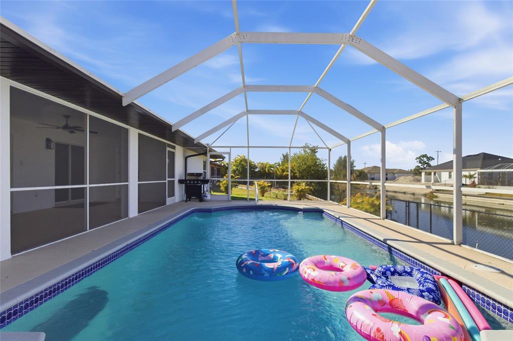 A screened-in swimming pool with floating rings sits on a patio overlooking a canal — 619 SW 26TH TERRACE, CAPE CORAL, FL